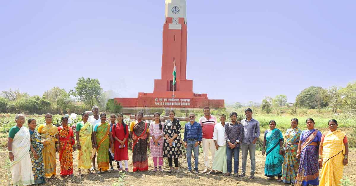 A group of farmers and students standing together in front of a red clock tower in an agricultural field